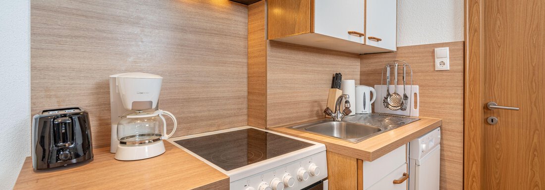 A modern kitchen with wood surfaces and white cabinets. On the countertop are a coffee machine, a kettle, and various kitchen utensils. - Pension Birkenheim - Sölden