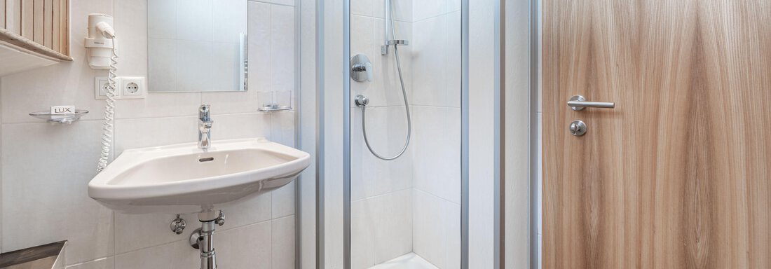 A modern bathroom with a shower cabin and a sink. The walls are brightly tiled and the wooden door is visible. - Pension Birkenheim - Sölden