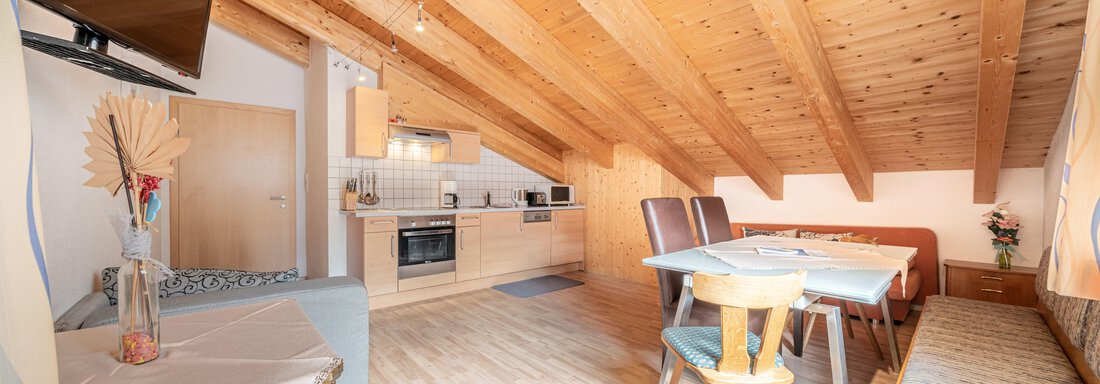 A bright and modern attic apartment with wooden beams. The space includes a kitchen, a dining area, and cozy seating. - Pension Birkenheim - Sölden