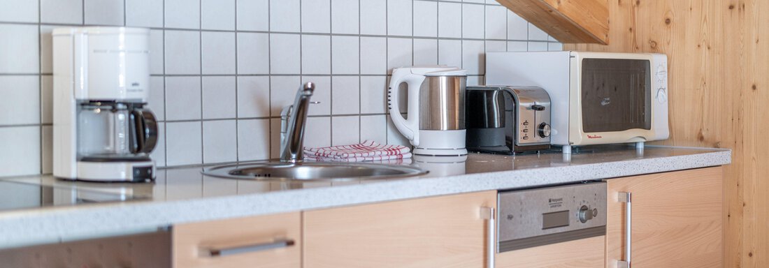 A modern kitchen with wood and tile elements. Various kitchen appliances such as a coffee machine, kettle, and microwave are visible. - Pension Birkenheim - Sölden