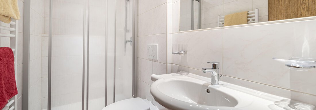 A modern bathroom with a shower and a sink. The walls are tiled in light colors, and there are towels in various colors. - Pension Birkenheim - Sölden