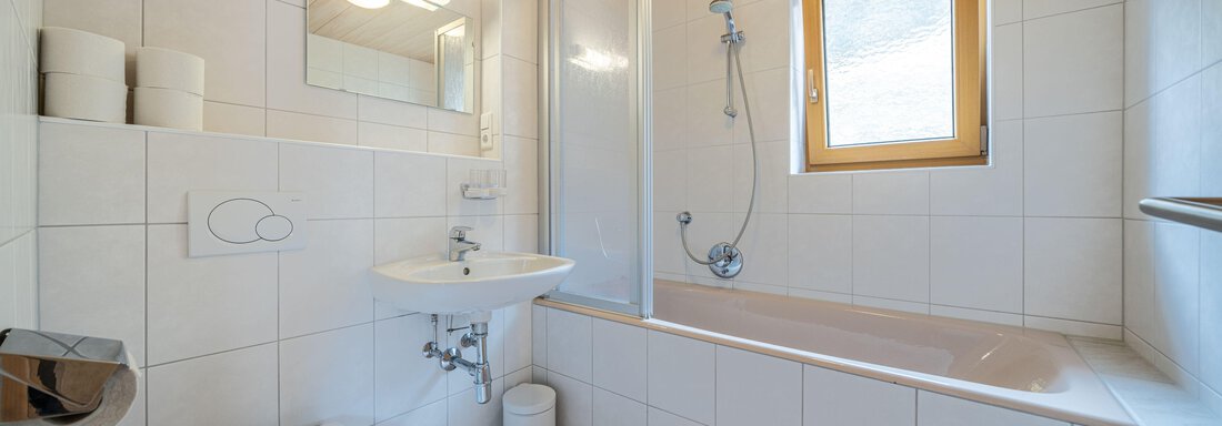 A modern bathroom with a bathtub and a separate shower. Bright tiles and a window create a pleasant atmosphere. - Pension Birkenheim - Sölden