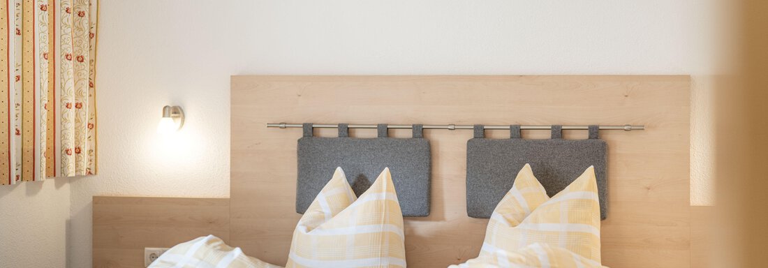A cozy bedroom with a large bed and pillows. The walls are designed in a bright and friendly manner. - Pension Birkenheim - Sölden