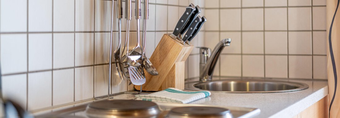 A modern kitchen with a sink and stove. It is equipped with cooking utensils and a knife block. - Pension Birkenheim - Sölden