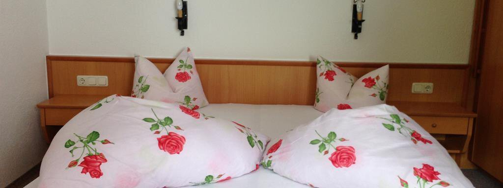 Zimmer A cozy bedroom with a double bed and pillows with a rose pattern. The walls are light and the lighting is soft. - Pension Birkenheim - Sölden