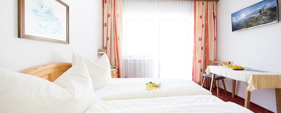 Doppelzimmer A bright room with two single beds and large windows. The furnishings are simple and cozy, with a table and a chair. - Pension Charly - Sölden