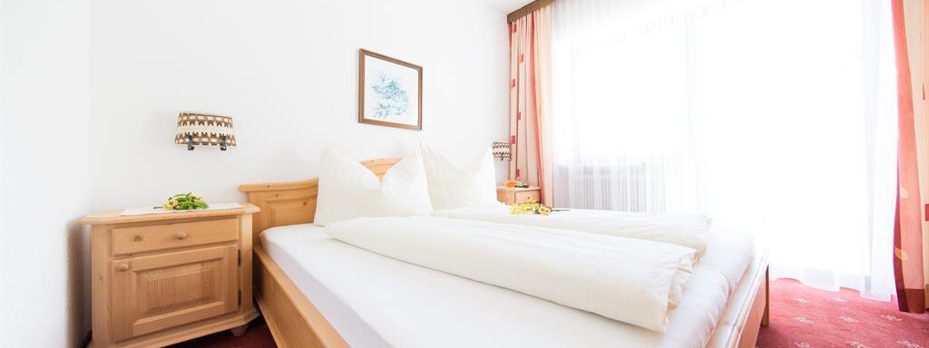 A cozy bedroom with two beds and large windows. The decor is bright and cheerful, perfect for a relaxing stay. - Pension Charly - Sölden