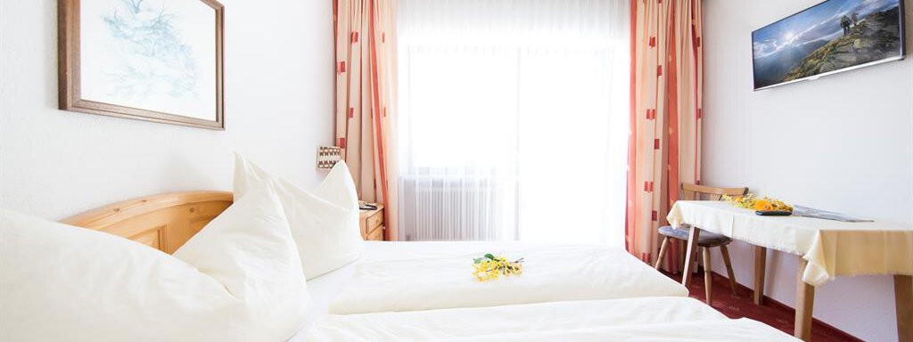 A cozy bedroom with two single beds and light furniture. Large windows provide plenty of light and a view outside. - Pension Charly - Sölden
