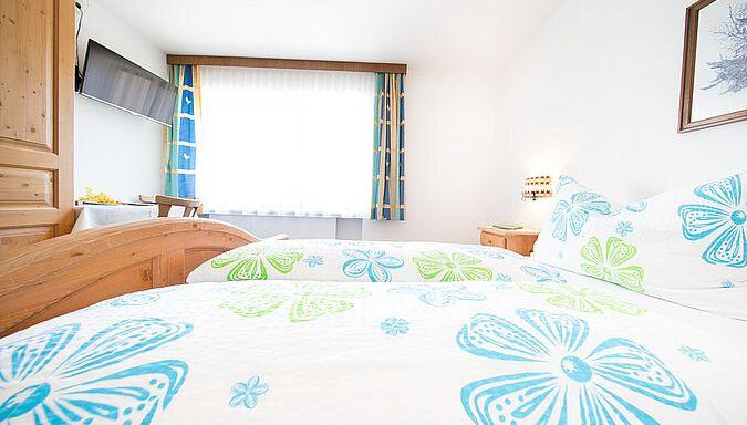 A bright room with a double bed and colorful bed covers. Large windows provide plenty of daylight. - Pension Charly - Sölden