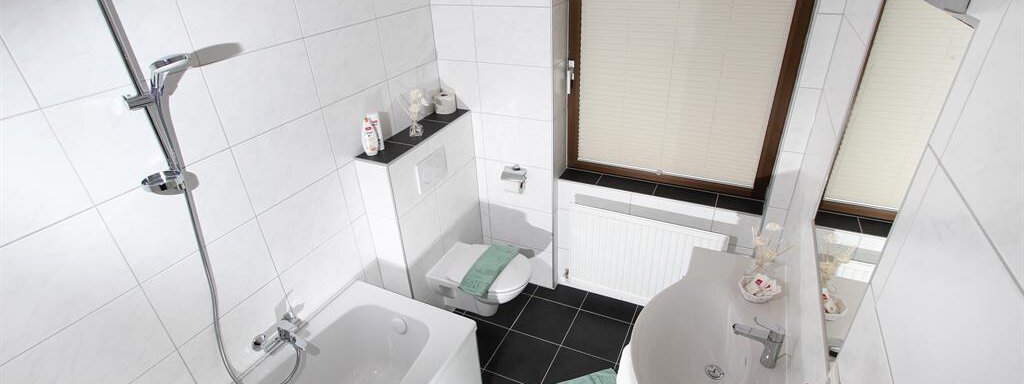 A modern bathroom with a bathtub and a shower. The walls are in light tiles, and there are fresh towels in mint green. - Pension Charly - Sölden