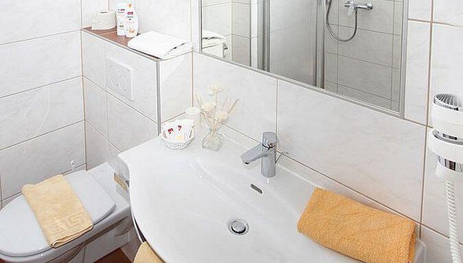 A modern bathroom with a shower, a sink, and a toilet. There are towels in orange and white as well as care products visible. - Pension Charly - Sölden