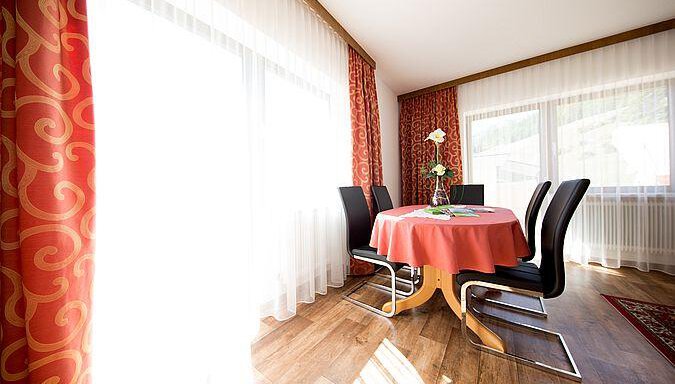 An elegant dining area with a round table and black chairs. Bright curtains let in plenty of light and give the room a friendly atmosphere. - Pension Charly - Sölden