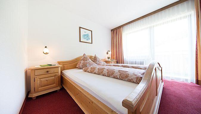 A cozy bedroom with a double bed and wooden wardrobes. Large windows let in plenty of daylight and offer a view outside. - Pension Charly - Sölden