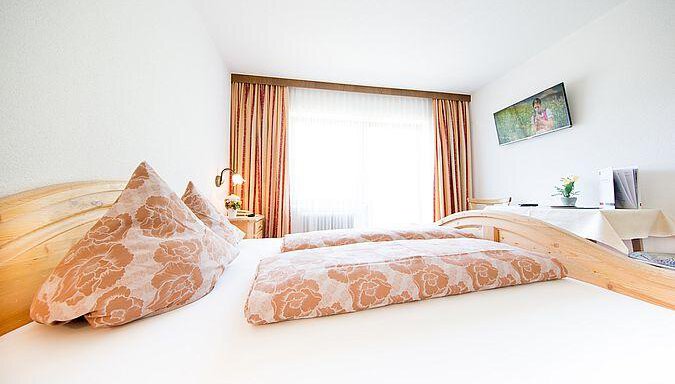 A bright and modern room with a cozy bed and nice pillows. Next to the bed is a television and a table with a small plant. - Pension Charly - Sölden