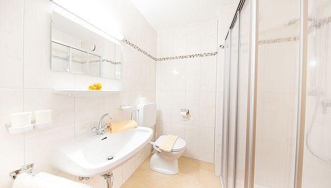 A modern bathroom with bright tiles and a white bathtub. There is a shower and a mirror above the sink. - Pension Charly - Sölden