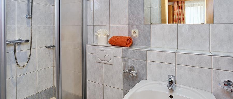 Badezimmer A modern bathroom with a shower, sink, and a toilet. The walls are covered with light, tile-like materials. - Pension Gritsch Ewald - Sölden