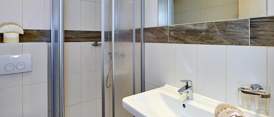 A modern bathroom with a shower and a sink. The walls are brightly tiled and there is a large bathroom mirror. - Pension Gritsch Ewald - Sölden