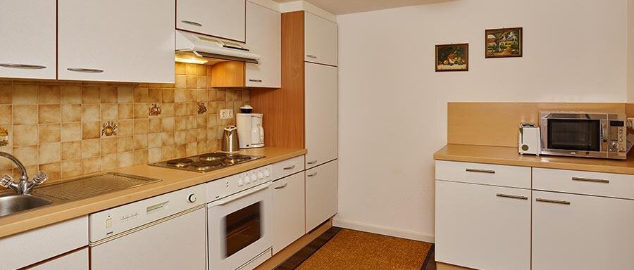 A modern kitchen with white kitchen furniture and wooden details. It is well equipped with appliances like a stove, a microwave, and a refrigerator. - Pension Gritsch Ewald - Sölden