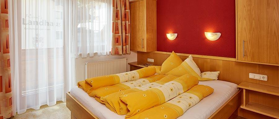 A cozy bedroom with a large bed and colorful pillows. The walls are painted in warm tones and there is plenty of daylight through the windows. - Pension Gritsch Ewald - Sölden