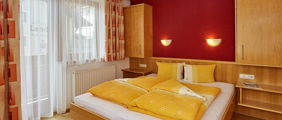 A cozy bedroom with a large bed and yellow pillows. Large windows provide plenty of daylight and a warm atmosphere. - Pension Gritsch Ewald - Sölden