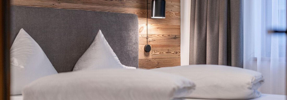 Doppelzimmer Edelweiss | © Pension Miramonte (CC C) A cozy bedroom with a wooden panel and two beds. The bedspreads are neatly turned down, and a soft light creates an inviting atmosphere. - Pension Miramonte - Sölden