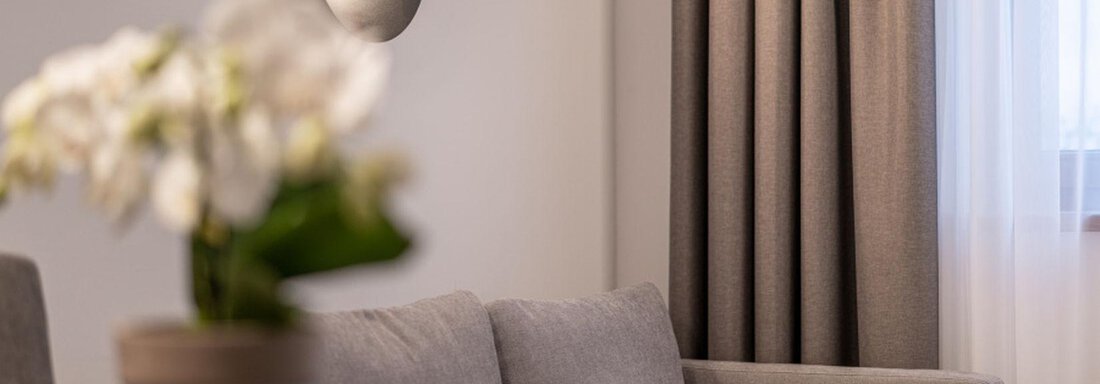 A modern living room with a gray sofa and soft light sources. A flower pot with a plant is on the table. - Pension Miramonte - Sölden