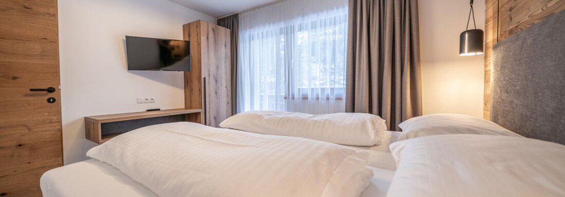 A modern bedroom with two cozy beds and a large window. The decor is simple and inviting, perfect for a relaxing overnight stay. - Pension Miramonte - Sölden