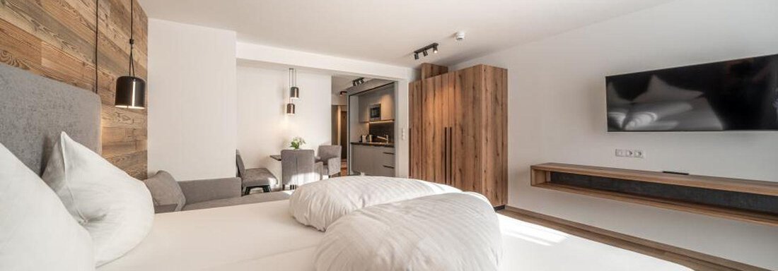 A modern bedroom with a double bed and bright wooden furniture. There is a TV on the wall as well as a cozy sitting area. - Pension Miramonte - Sölden