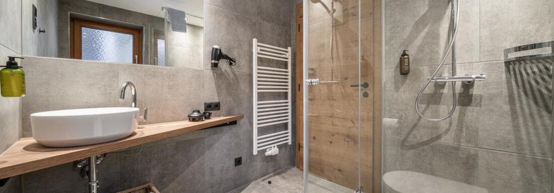 A modern bathroom with a glass shower and wooden elements. The large tiles make the space feel spacious and inviting. - Pension Miramonte - Sölden