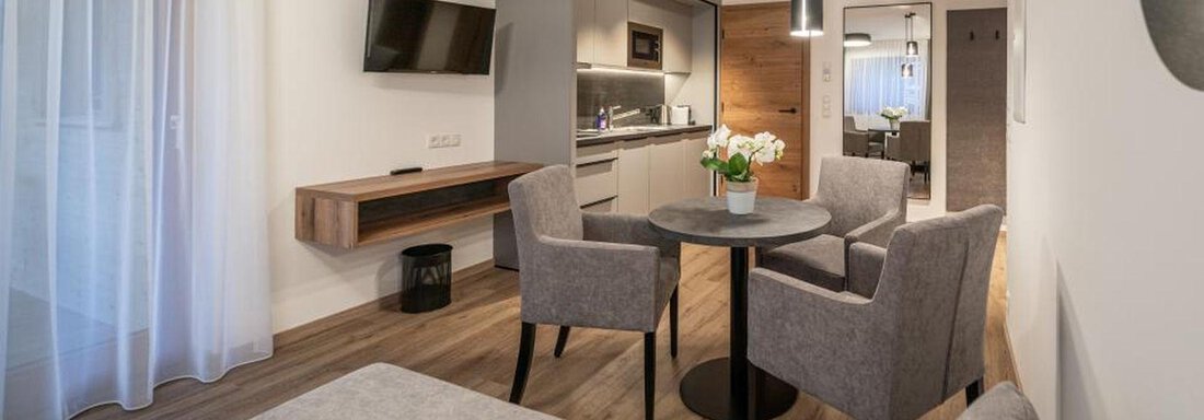 A modern living room with a cozy seating area and a dining table. The room is brightly and cheerfully designed, with an open kitchen in the background. - Pension Miramonte - Sölden