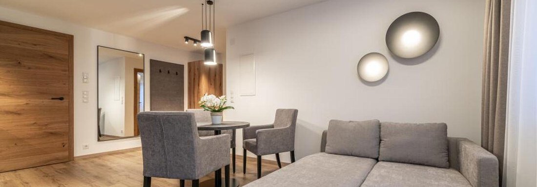A modern living room with a gray sofa and a small table. The room has bright walls and a cozy wooden floor. - Pension Miramonte - Sölden