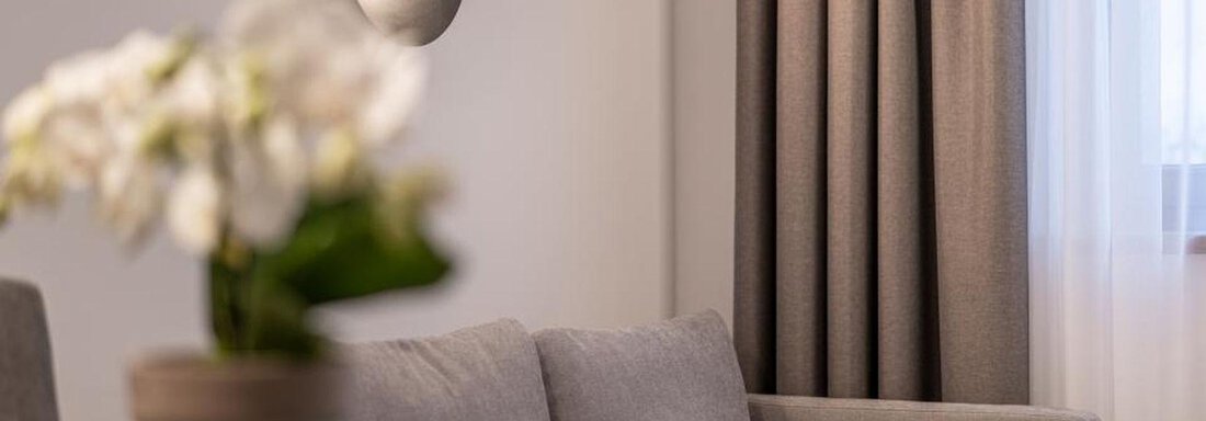 A cozy seating area with a gray sofa and a modern lamp on the wall. There is a flower pot with white flowers on a table. - Pension Miramonte - Sölden