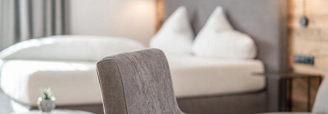 A modern hotel room with a cozy double bed and an armchair. The walls are made of wood and the ambiance is bright and inviting. - Pension Miramonte - Sölden