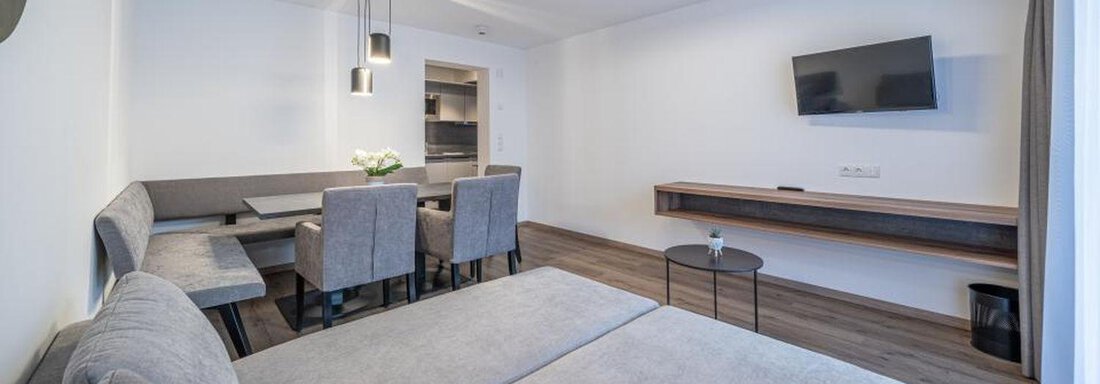 Appartement Alpenrose | © Pension Miramonte (CC C) A modern living and dining room with a gray couch and a table for four people. The room has bright walls and a flat-screen TV. - Pension Miramonte - Sölden