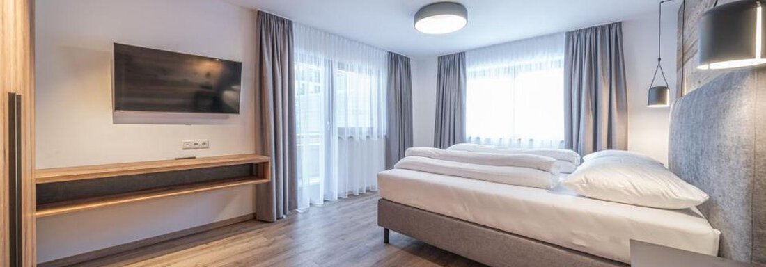 A modern room with a double bed and a flat-screen TV. Large windows let in plenty of daylight. - Pension Miramonte - Sölden