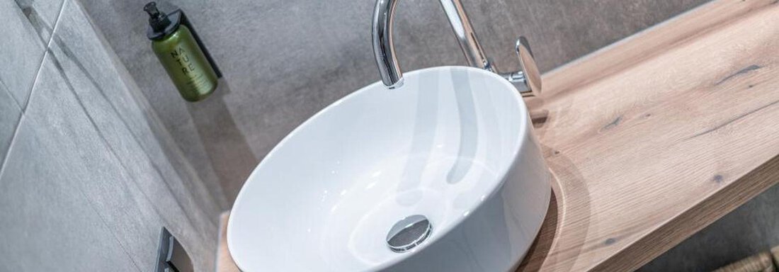 A modern ceramic sink on a wooden panel. Towels in a basket are visible in the background. - Pension Miramonte - Sölden