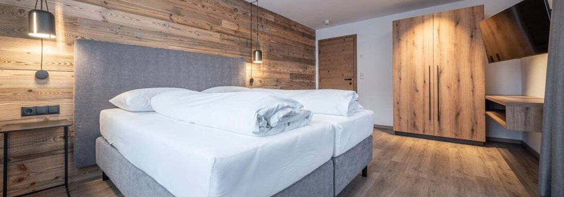 A modern bedroom with a large bed and wooden walls. The cozy atmosphere is complemented by soft lighting and a desk area. - Pension Miramonte - Sölden
