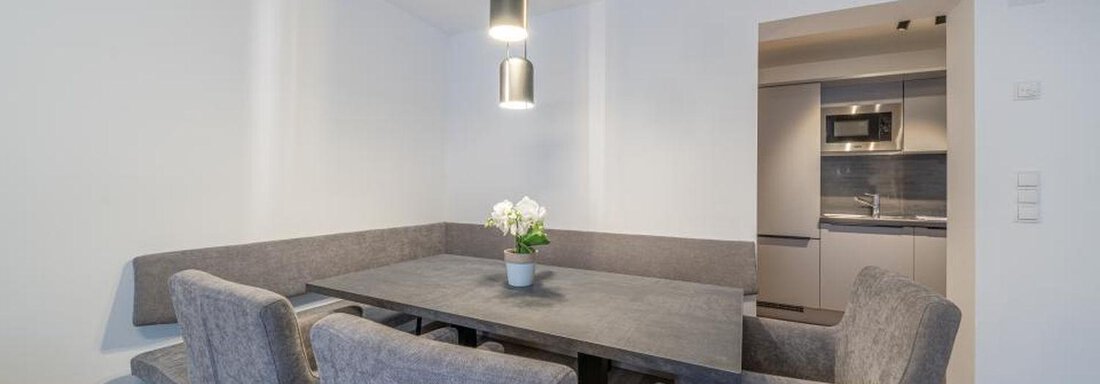 A modern dining area with a gray table and comfortable chairs. In the background, an open kitchen is visible. - Pension Miramonte - Sölden
