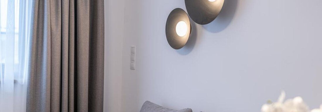 A modern living room with gray curtains and a beige sofa. Two round lamps are hanging on the wall, emitting warm light. - Pension Miramonte - Sölden