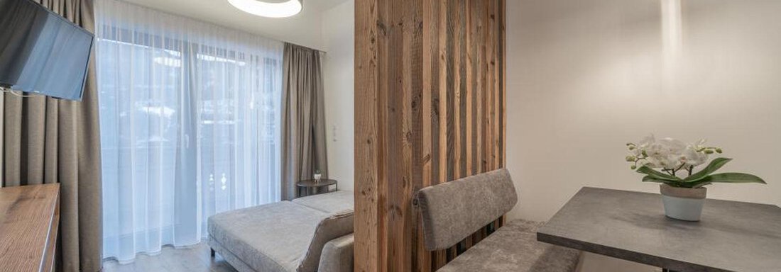 Wohnraum Enzian | © Pension Miramonte (CC C) A modern room with wood paneling, a comfortable bed, and a small table. Large windows provide plenty of daylight. - Pension Miramonte - Sölden