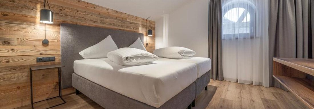 A modern bedroom with a comfortable double bed and wooden decor. The room has large windows and a warm, inviting style. - Pension Miramonte - Sölden