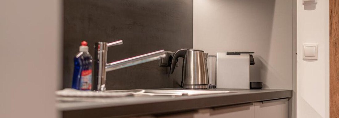 A modern kitchen with a kettle, a sink, and a white coffee machine. The walls are in neutral colors and the lighting creates a pleasant atmosphere. - Pension Miramonte - Sölden