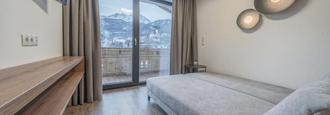 A modern room with a cozy sofa bed and large windows. The view overlooks the mountains and the balcony railing is visible. - Pension Miramonte - Sölden