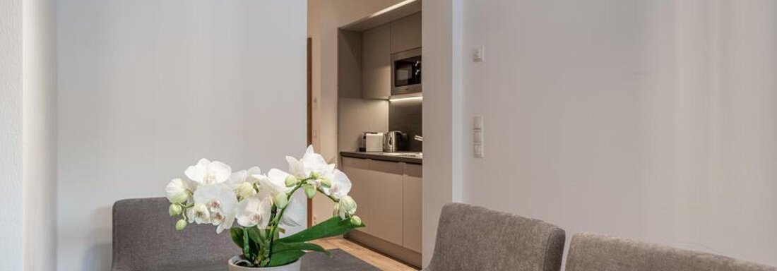 A modern dining area with a table and gray chairs. On the table, there is a pot with white orchids. - Pension Miramonte - Sölden