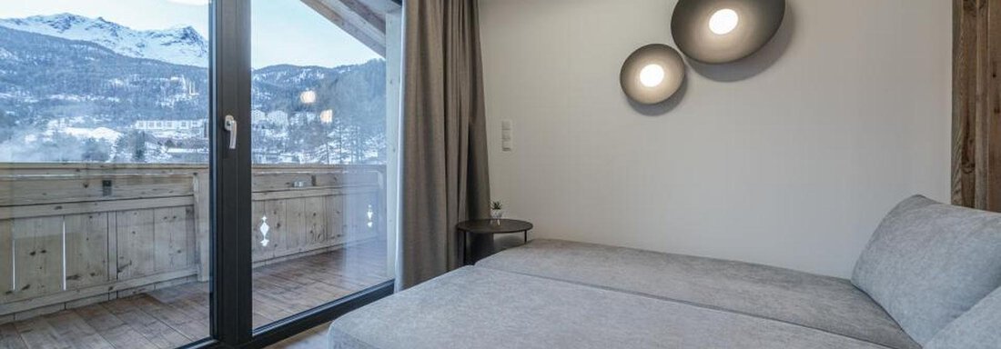 A modern room with a gray sofa and large windows. Outside, a beautiful mountain landscape can be seen. - Pension Miramonte - Sölden