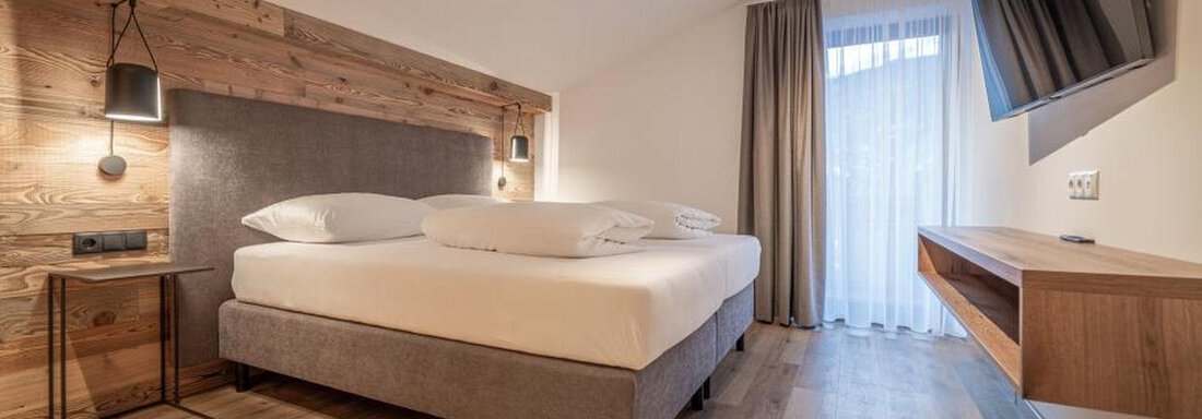 A modern bedroom with a large bed and wooden paneling. The room has plenty of daylight and a cozy atmosphere. - Pension Miramonte - Sölden