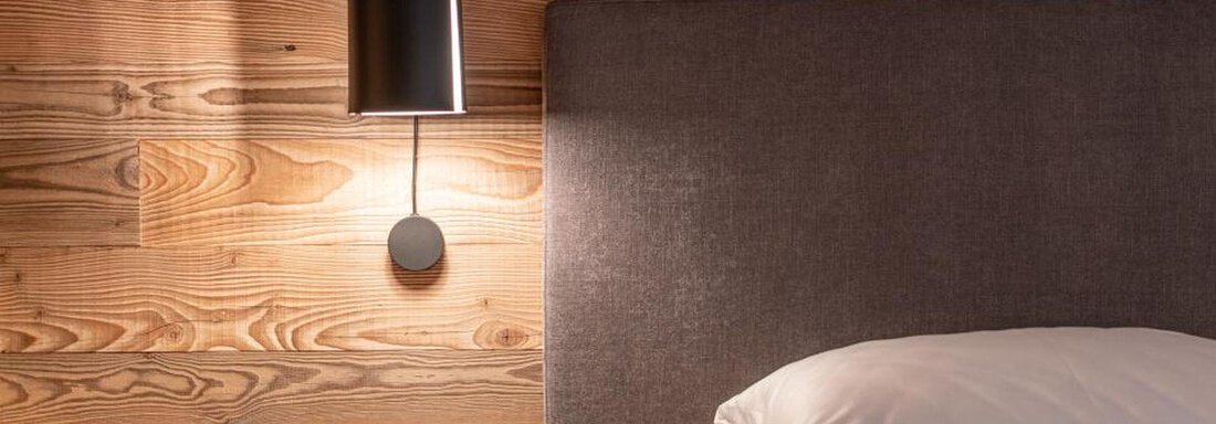 A modern bedroom with a cozy bed and a stylish lamp. The wood paneling creates a warm atmosphere. - Pension Miramonte - Sölden