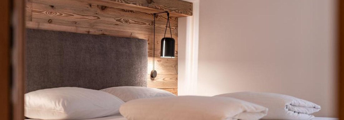 A cozy bedroom with a modern bed and wooden details. The light creates an inviting atmosphere. - Pension Miramonte - Sölden