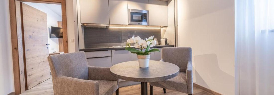 Wohküche im Appartement Arnika | © Pension Miramonte (CC C) A cozy living area with a round table and two chairs. In the background, there is a modern kitchenette. - Pension Miramonte - Sölden