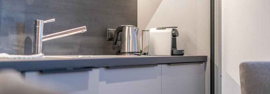 A modern kitchen unit with a kettle and a coffee machine. The surface is dark and smooth, featuring a minimalist design. - Pension Miramonte - Sölden